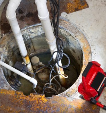 Repairing a sump pump in a basement with a red LED light illuminating the pit and pipe work for draining ground water